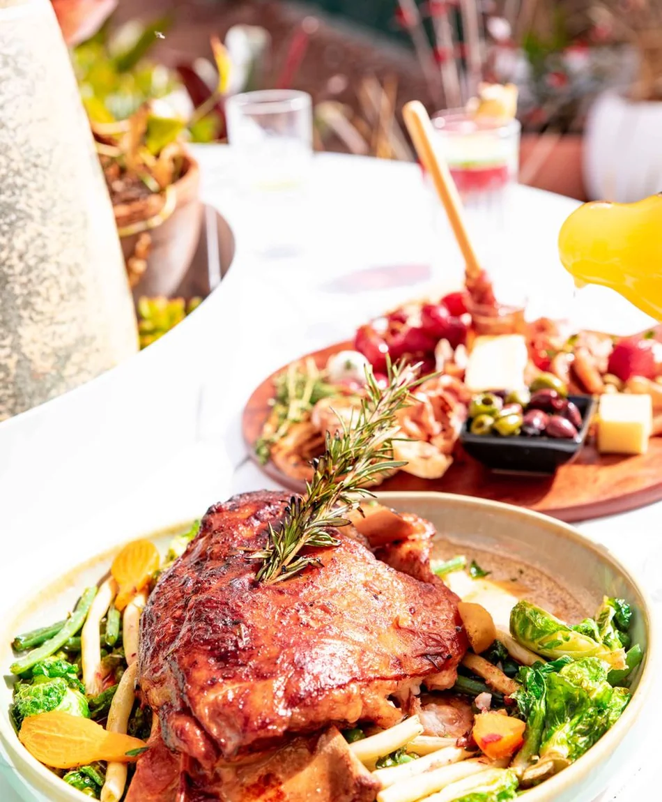 A plated spread of roasted meats and greens on an outdoor table, representative of a shared buffet dinner