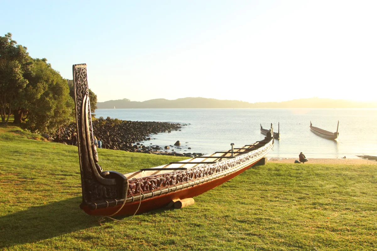 The carved ceremonial waka Ngātokimatawhaorua resting on the grass above the beach at Waitangi in golden evening light